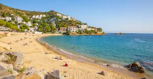 Fontanero Canyelles reparando tubería en calle típica con casas mediterráneas y paisaje montañoso de fondo