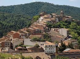 Fontanero Santa Maria d'Oló, calle con casas de piedra y montaña al fondo en día soleado