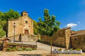 Fontanero Tavèrnoles en calle adoquinada con casas de piedra y fondo de colinas verdes en el centro del pueblo.